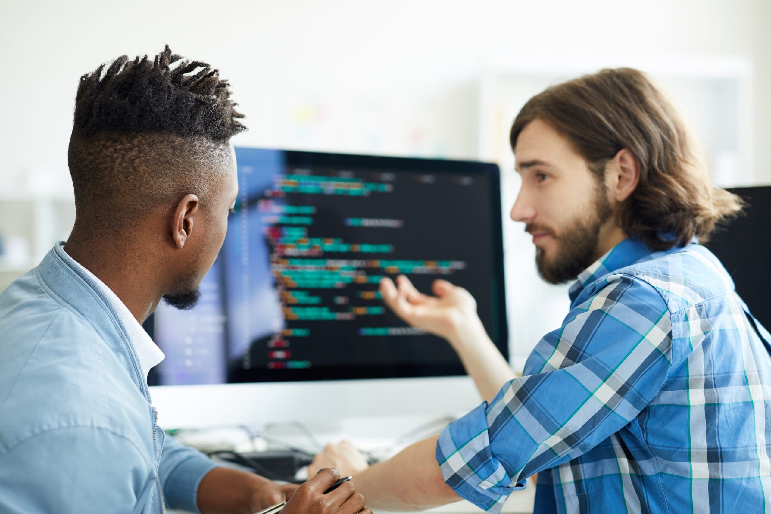 Two IT experts in Springfield discuss code on a monitor, collaborating on managed IT services in a modern office setting.