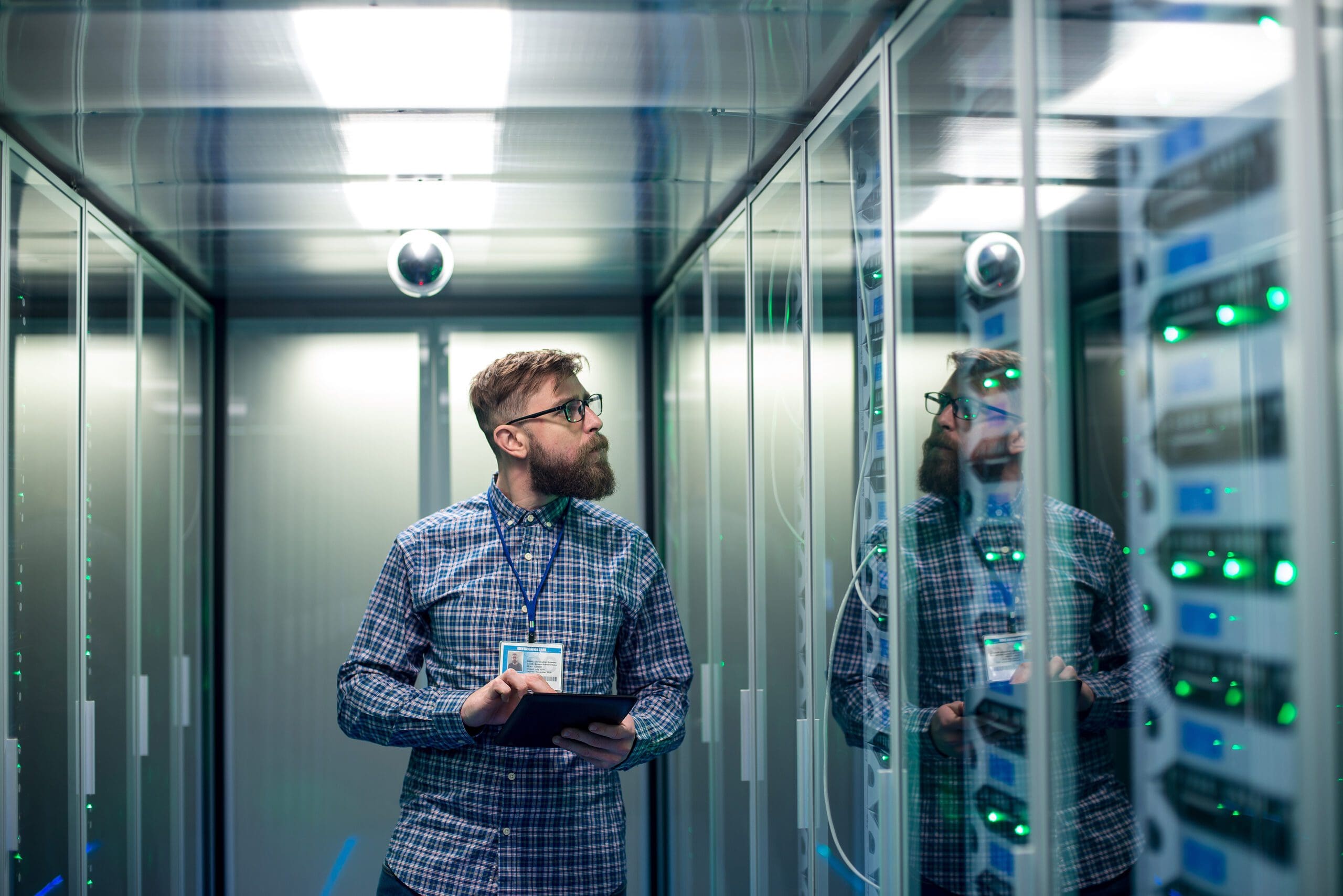 Wide shot of casual man with tablet walking among server racks in data center room looking at hardware
